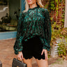 A close-up of a fashionable green velvet top with a bold pattern, paired with scalloped shorts, showcasing a modern take on classic textures and silhouettes.