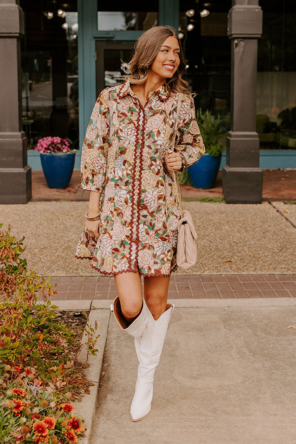 Full-length view of a woman in a beautiful green floral dress with white and pink flower accents, complemented by white cowboy boots, radiating an effortlessly chic vibe.