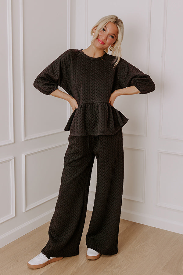 Woman wearing a cozy black quilted two-piece lounge set with a peplum top and wide-leg pants, styled with white sneakers.